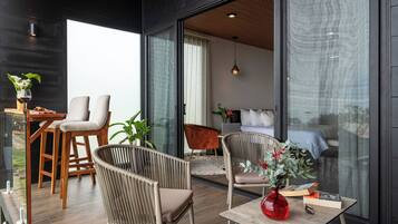 Una sala de estar moderna con un ventanal que da a un dormitorio, una mesa de comedor de madera con sillas y un florero rojo sobre una mesita auxiliar.
