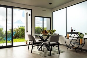 A modern dining area with a glass table, four chairs, and a black metal shelf with a vase. - ÉWA Homes Monteverde  (Monteverde)