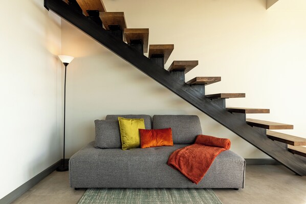 A modern living room with a grey sofa, a wooden staircase, and a floor lamp. - ÉWA Homes Monteverde (Monteverde)