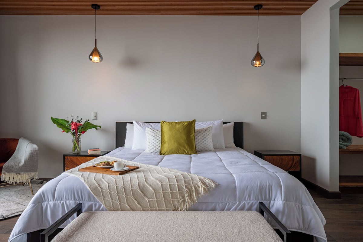 A modern bedroom with a large bed, two bedside tables, a nightstand, a chair, and a hanging light fixture.