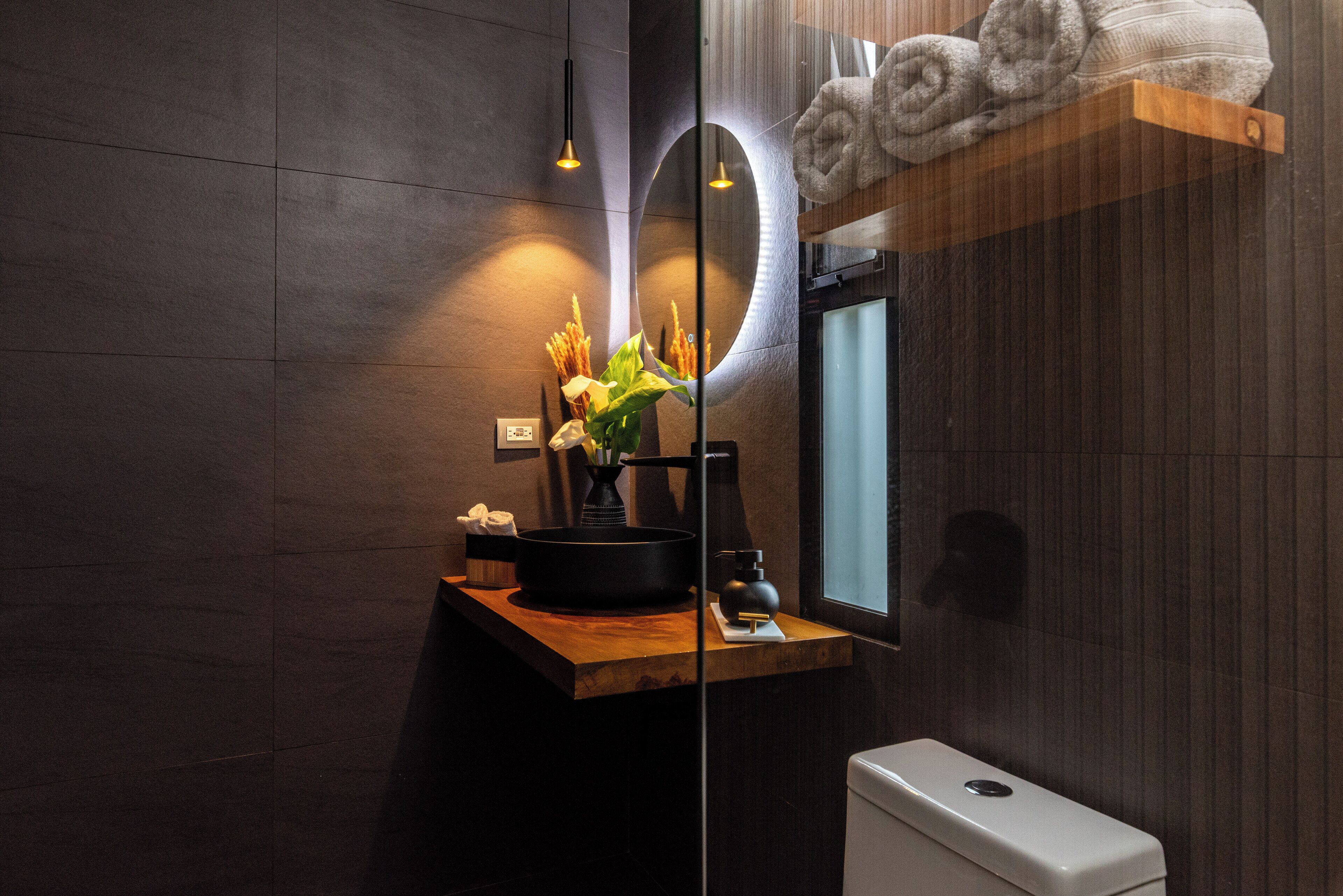 A modern bathroom with a wooden vanity, a black sink, a mirror, and a towel rack.
