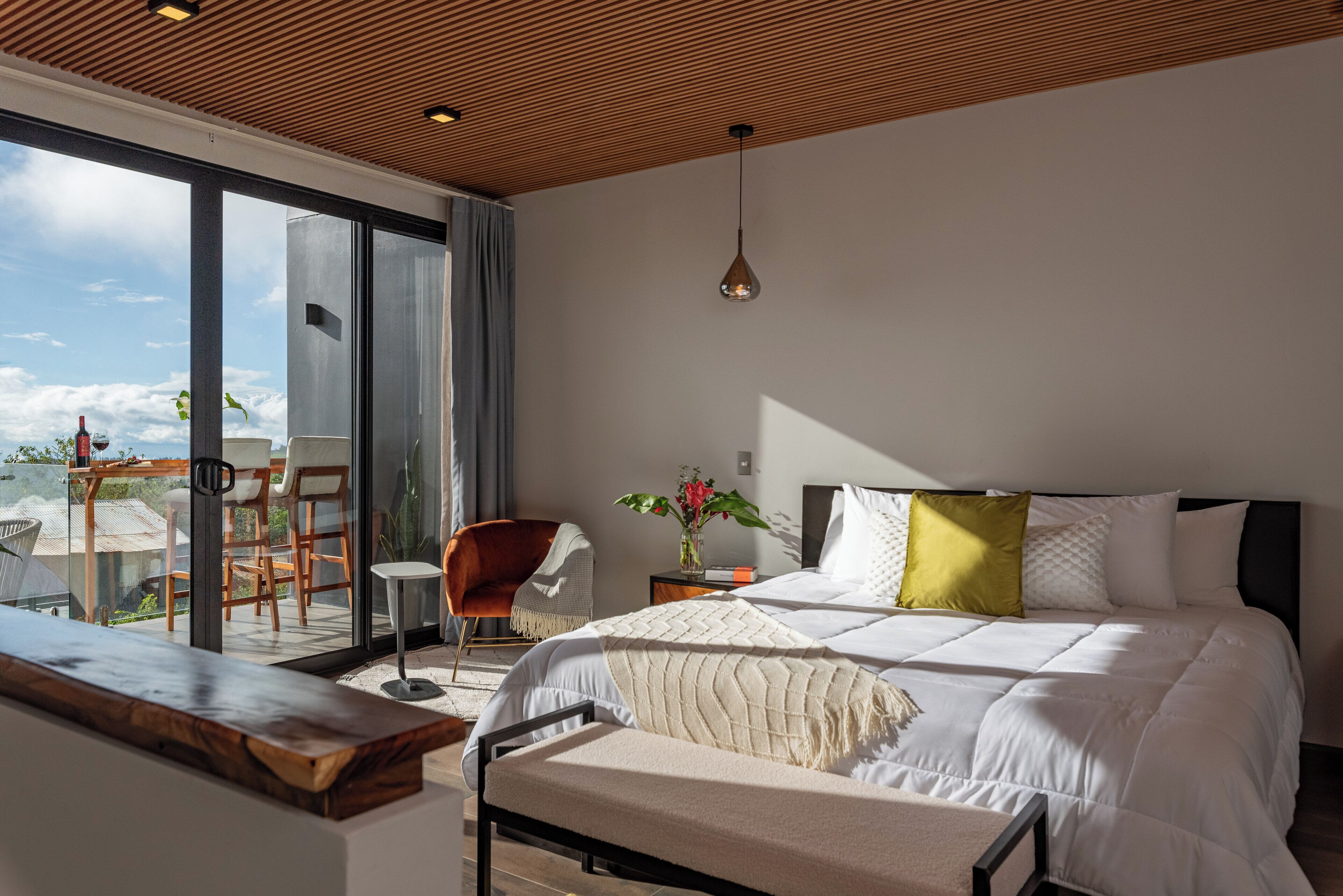 Une chambre moderne avec un grand lit, un plafond en bois et une vue sur l’extérieur.
