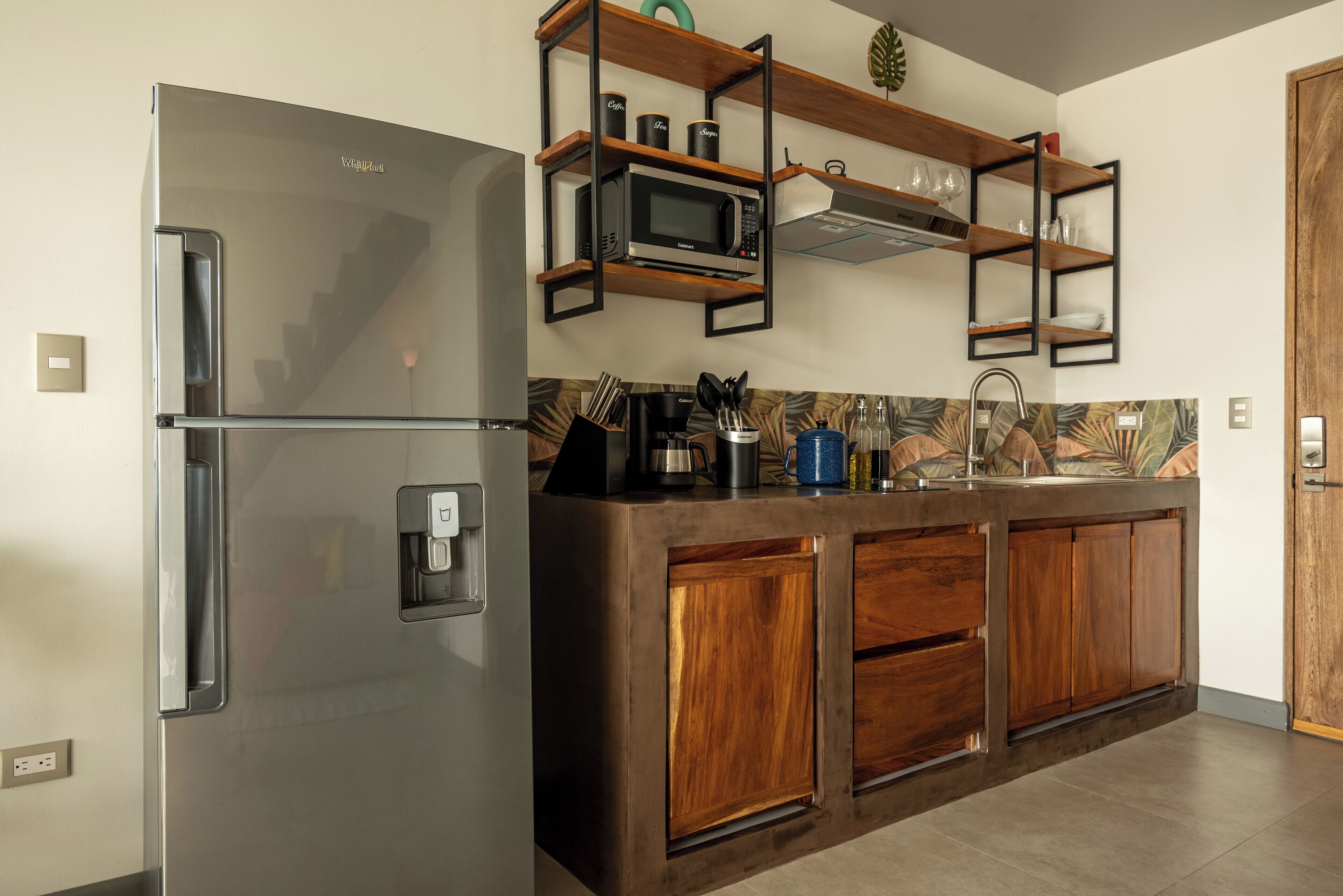 A kitchen with a stainless steel refrigerator, wooden cabinets, a microwave, and a coffee machine.