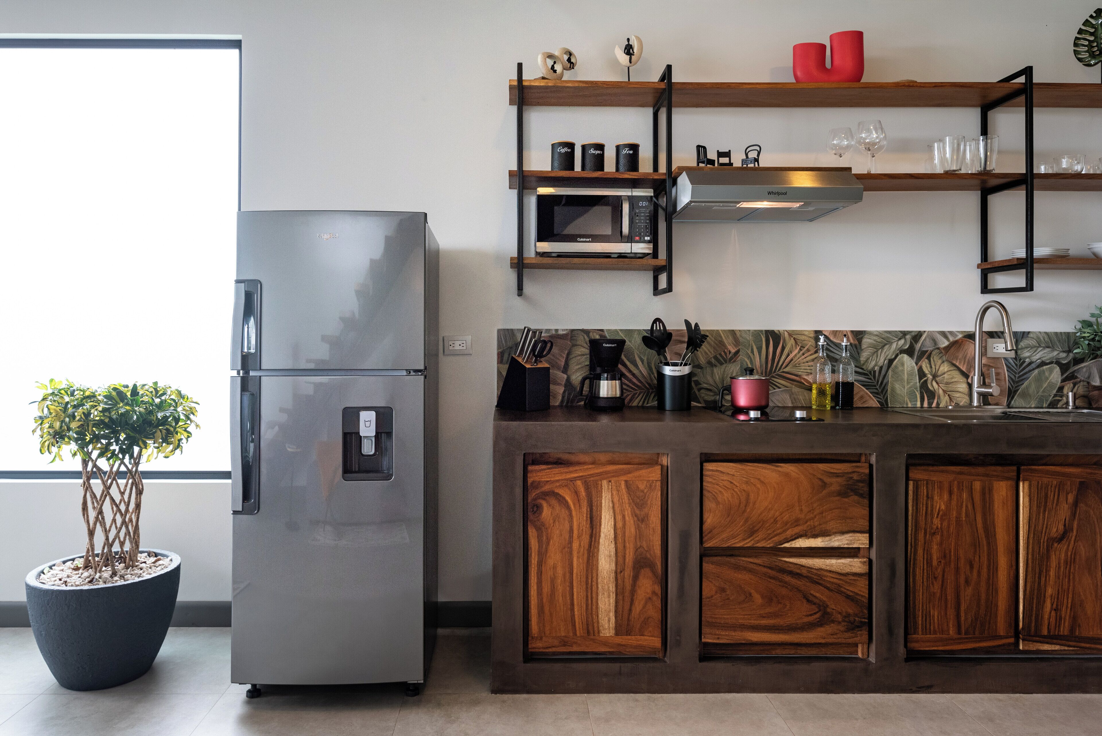 Una cocina moderna con un refrigerador de acero inoxidable, armarios de madera, un microondas y una cafetera.