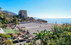 A beach with a stone tower, umbrellas, and outdoor seating. - Luxurious home in Almuñecar with private swimming pool, can be inside or outside (Almuñecar)
