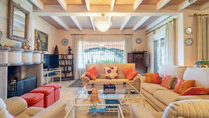 A spacious living room with a sofa set, a coffee table, and a television. There are decorative items on shelves and a chandelier hanging from the ceiling. - Awesome home in Almuñecar (Almuñecar)