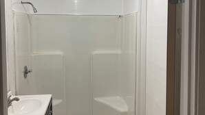 Un baño pequeño con azulejos blancos, con cabina de ducha, lavamanos e inodoro.