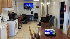 Una cocina con estufa, microondas y armarios. Hay un televisor montado en la pared, un extintor y una mesa con sillas.