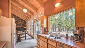 A modern kitchen with wooden cabinets, a large window offering a view of trees, and a built-in stove. - 5BR. Hot Tub! Full resort access (Sisters)