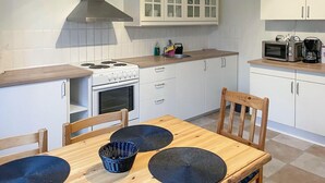 A kitchen with white cabinets, a stove, a microwave, and a dining table with chairs. - Nice apartment in Hyltebruk with WiFi (Hyltebruk)