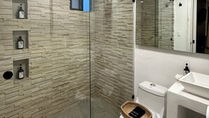 Een moderne badkamer met een douchecabine van glas, een wit toilet en een wastafel met een grote spiegel erboven.