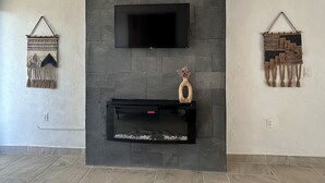 Een moderne woonkamer met een stenen openhaard, een flatscreen televisie erboven en twee wanddecoraties van macramé.