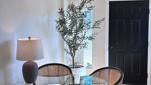 Un comedor con mesa de vidrio, sillas de mimbre, una planta en maceta y una lámpara.