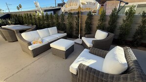 Un espacio al aire libre con patio amoblado con muebles de mimbre, incluyendo sofás y una mesa, y una sombrilla grande que proporciona sombra.