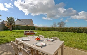 Un área de comedor al aire libre con una mesa preparada para cuatro, una parrilla y una casa al fondo.