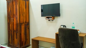 Een kamer met een houten kledingkast, een flatscreen televisie aan de muur, een bureau met een stoel en een waterfles op het bureau.