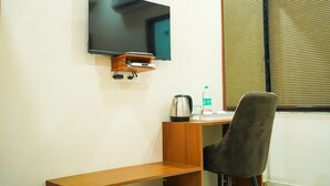 Een hotelkamer met een flatscreen televisie aan de muur, een houten bureau met een waterkoker, een fles water en een stoel.