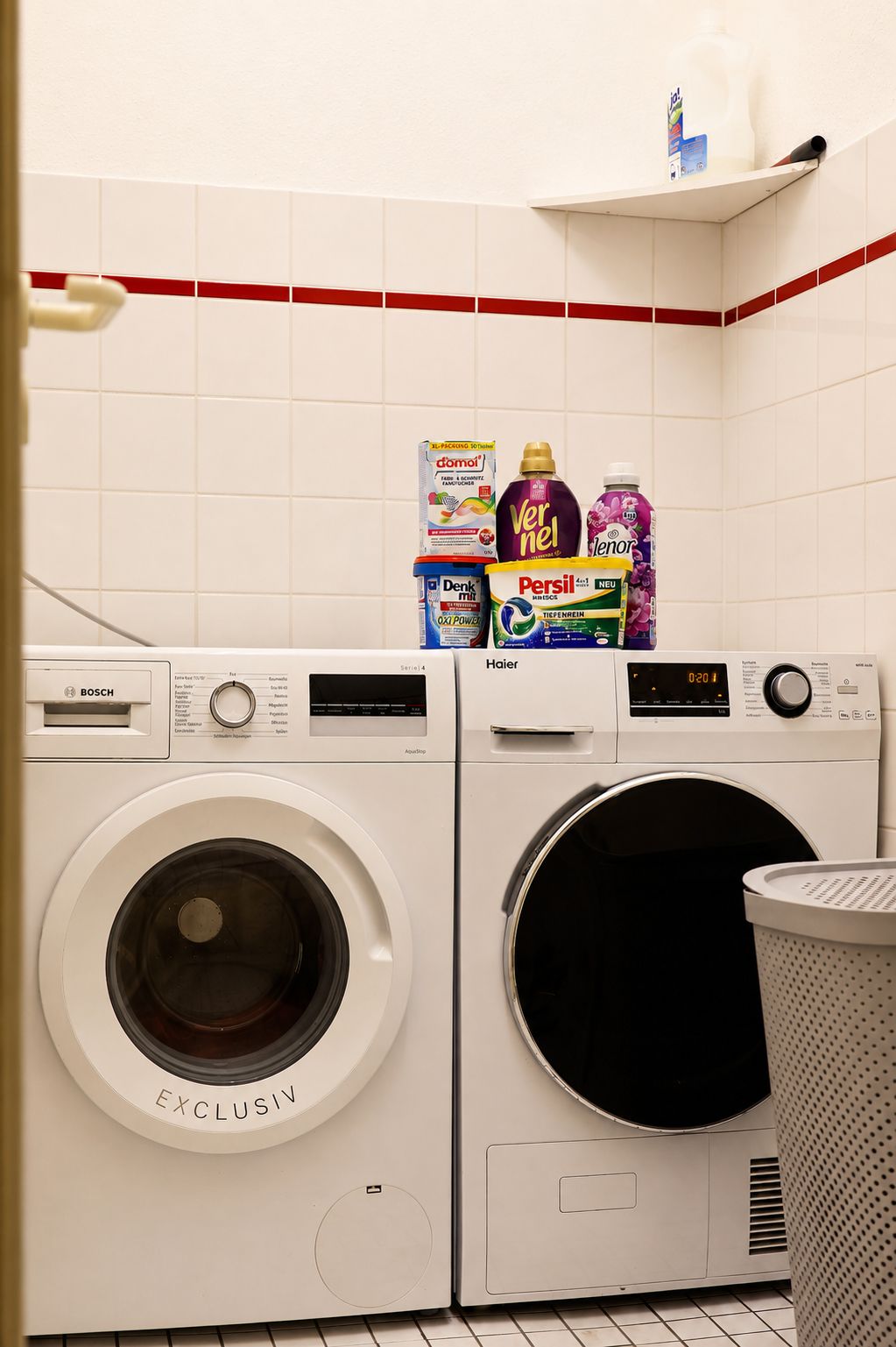 Un área de lavandería con dos lavadoras Bosch, un estante para detergente y un cesto de basura.