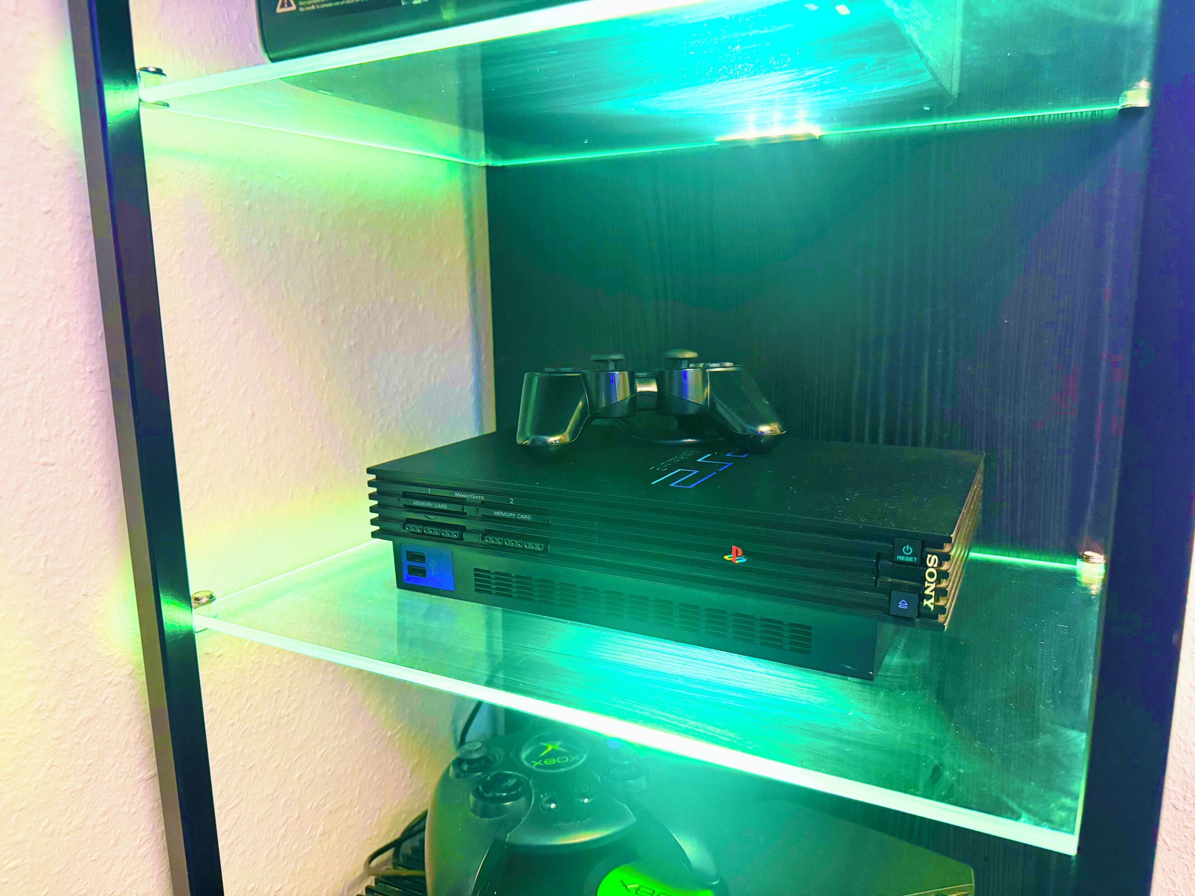 Ein Gaming-Einrichtung mit einer PS4, einem Controller und einem Monitor in einer Vitrine.