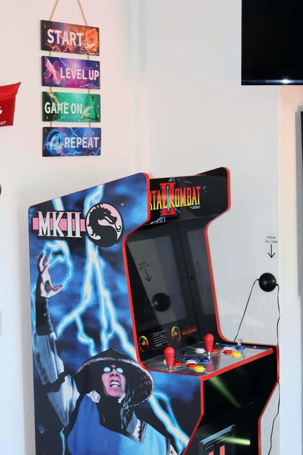 En arkadmaskin i retrostil med en karaktär från Mortal Kombat, en väggmonterad skylt med spelinstruktioner och en tv.