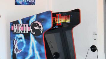 En arkadmaskin i retrostil med en karaktär från Mortal Kombat, en väggmonterad skylt med spelinstruktioner och en tv.