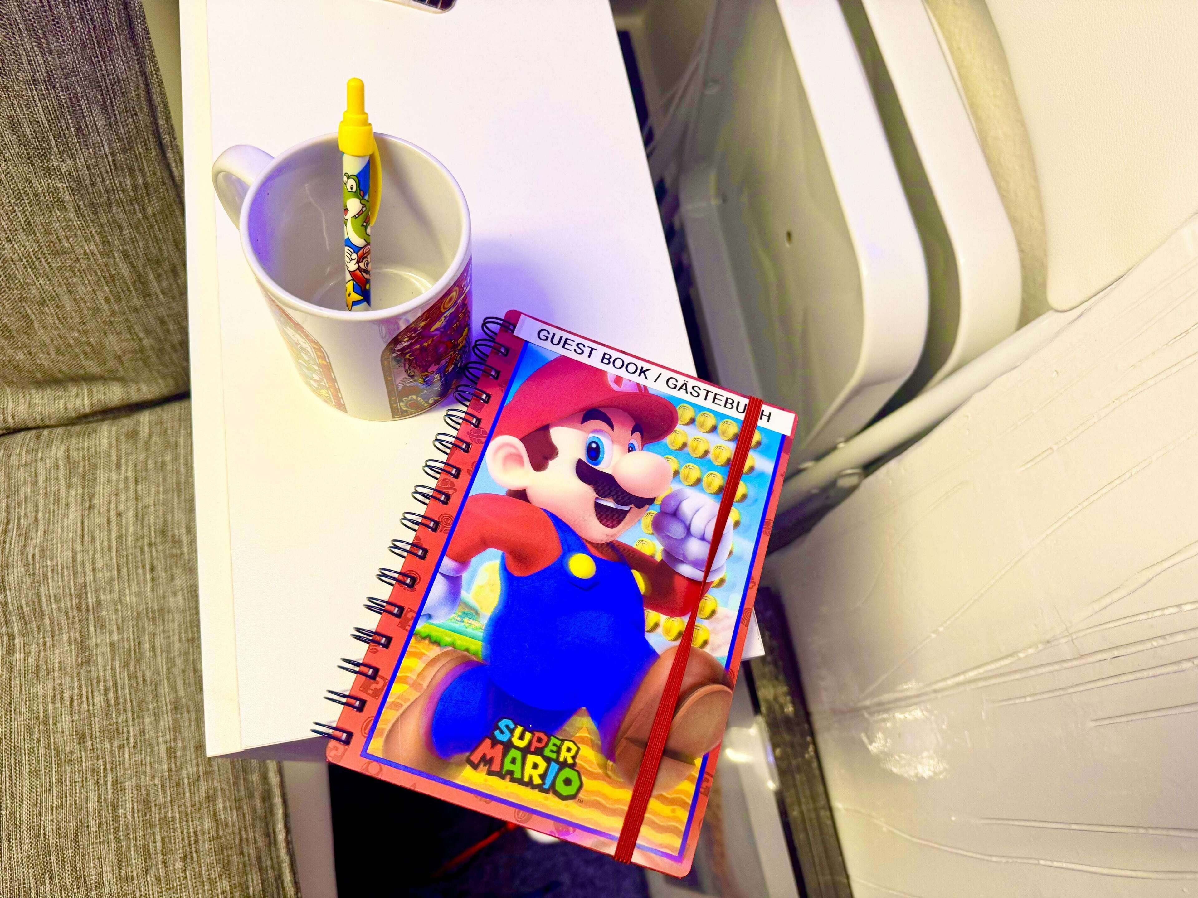 A notebook with a Super Mario character on the cover, a pen, and a mug on a table.