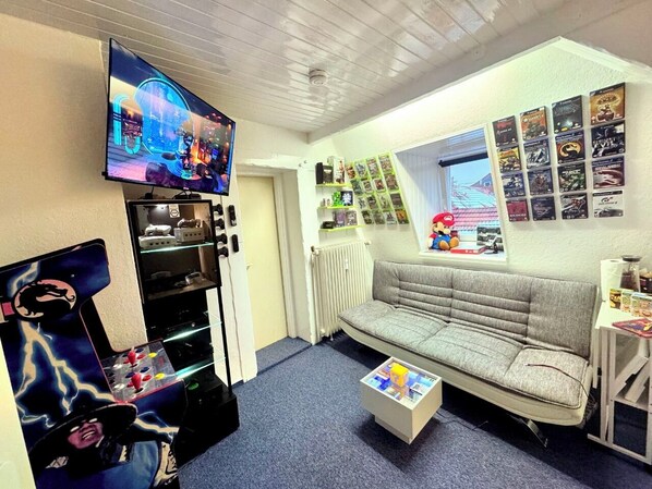A living room with a TV, gaming console, sofa, coffee table, and a wall with framed pictures. - 🎮Gamer's Lair🕹 incl. Extras (Göttingen)