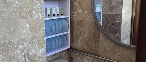 A bathroom with a toilet, a shelf with toiletries, a towel rack, and a mirror.