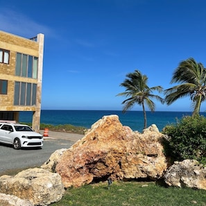 A building with a modern design, a white car parked in front, and a large rock formation. - Vacation Rental Arecibo PR (Arecibo)