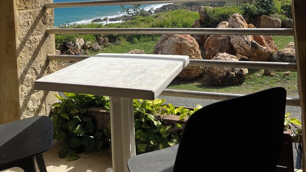 Un balcón con mesa y sillas, con vistas al mar, rocas y vegetación.