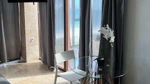 Una habitación moderna con una mesa de vidrio, sillas blancas, un sofá y un televisor instalado en la pared.