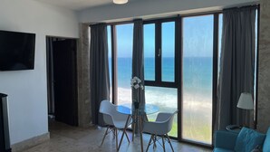 Una habitación con un ventanal que ofrece vista al mar, ventilador de techo, mesa de comedor con sillas y un sofá.