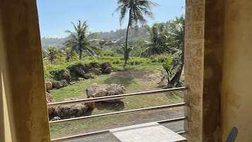Varanda com duas cadeiras e uma mesa, com vista para uma paisagem natural com palmeiras e pedras.
