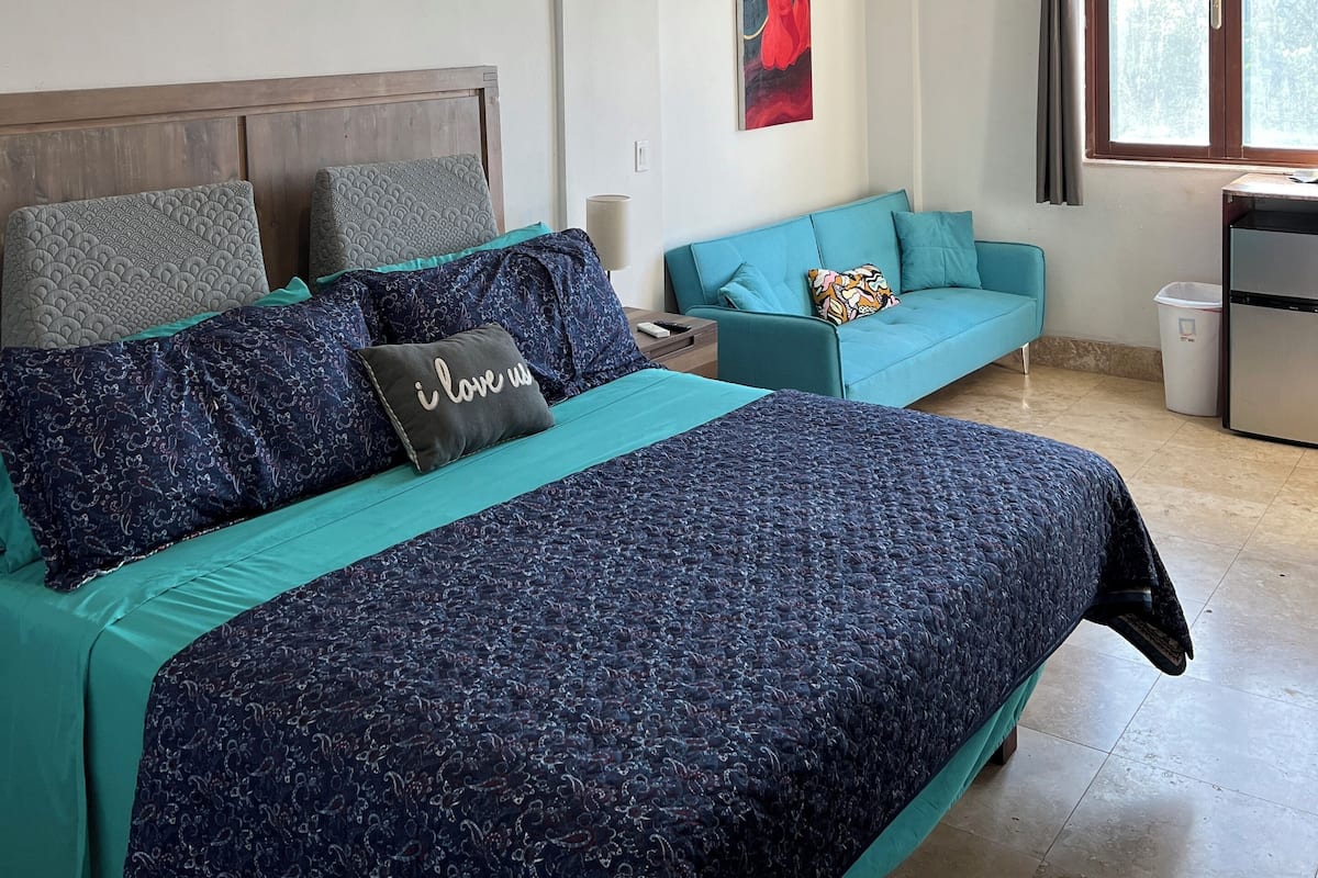 Quarto com uma cama, sofá, mesa pequena e janela.