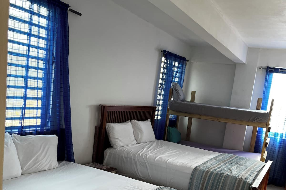 Quarto com duas camas, incluindo uma beliche, e uma janela com cortinas azuis.