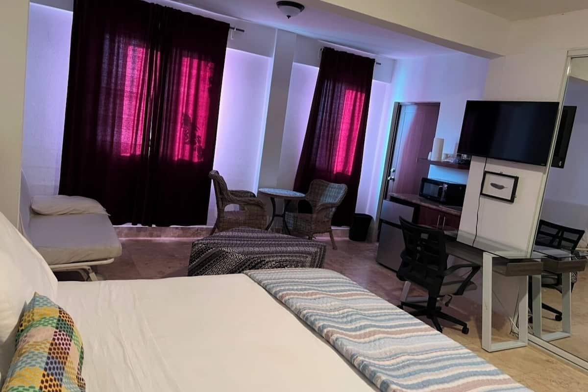 Quarto de hotel com cama, duas poltronas, escrivaninha com computador, televisão e micro-ondas.