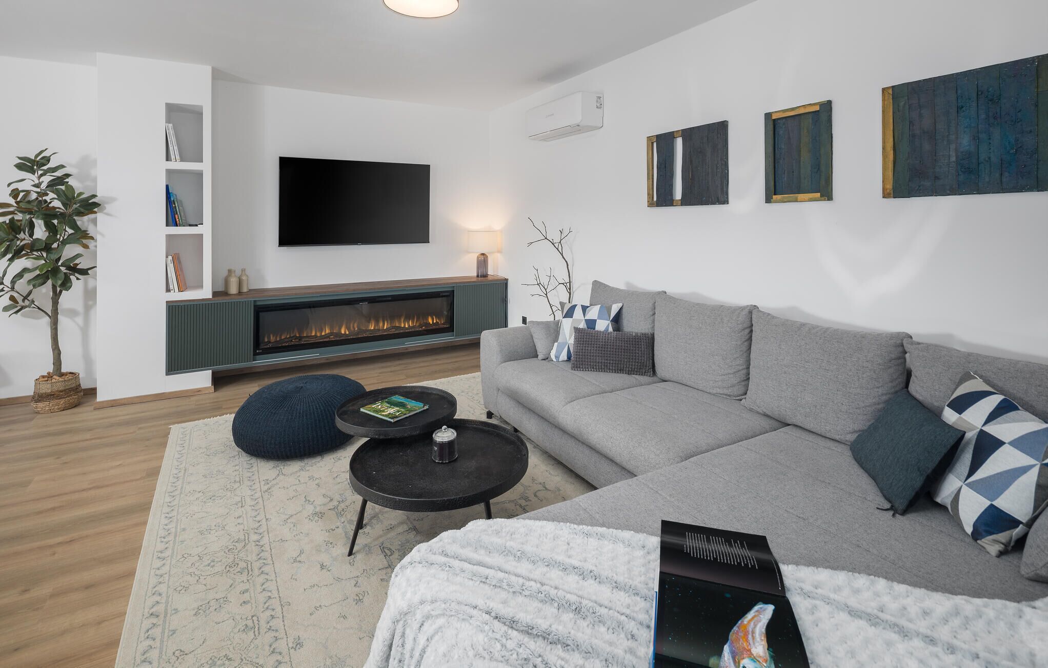 Ett modernt vardagsrum med en grå soffa, en platt-TV, en öppen spis och en bokhylla.