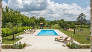 A swimming pool with lounge chairs and a children's play area, surrounded by greenery and stone walls.