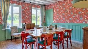 A dining area with a wooden table set for six, surrounded by red chairs with green cushions.
