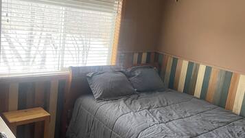 A bedroom with a bed, a desk, a ceiling fan, and a window with blinds.