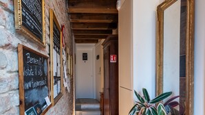 A narrow hallway with a stone wall, wooden beams, and a wooden cabinet with a plant. There are framed pictures and a chalkboard with text. - Historic housing in pedestrian square - Borgo Portello (Padova)