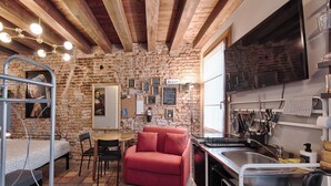 A compact kitchen with a red sofa, a dining table, and a TV mounted on the wall. - Historic housing in pedestrian square - Borgo Portello (Padova)