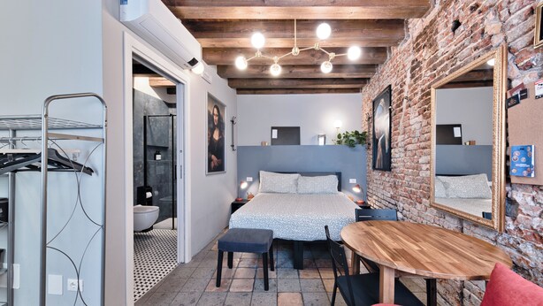 A compact bedroom with a bed, bedside tables, a mirror, and a small wooden table. - Historic housing in pedestrian square - Borgo Portello (Padova)