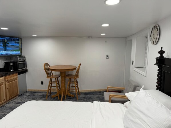A hotel room with a bed, a small table with chairs, a TV, a clock, and a microwave. - Cozy 1-bedroom apartment in charming Schenectady just renewed has AC HEAT WIFI (Schenectady)
