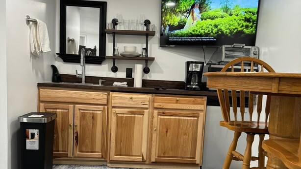 Eine moderne Küche mit Holzschränken, einem eingebauten Backofen, einer Kaffeemaschine und einem Fernseher, der über der Arbeitsfläche angebracht ist.