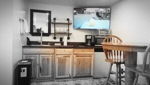 Eine Küche mit Holzausstattung, fest eingebautem Backofen, einer Kaffeemaschine und einem Fernseher, der über dem Backofen installiert ist und eine Szene zeigt.