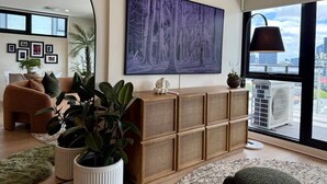 Uma sala de estar moderna com uma grande janela, um quadro pendurado, um sofá, uma mesa de centro e um aparador decorativo.