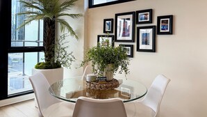 Uma sala de jantar moderna com mesa de vidro, cadeiras brancas e uma grande planta em vaso.