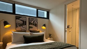 Uma cama bem arrumada com um cobertor verde, duas luminárias pretas em cada lado e uma obra de arte na parede.