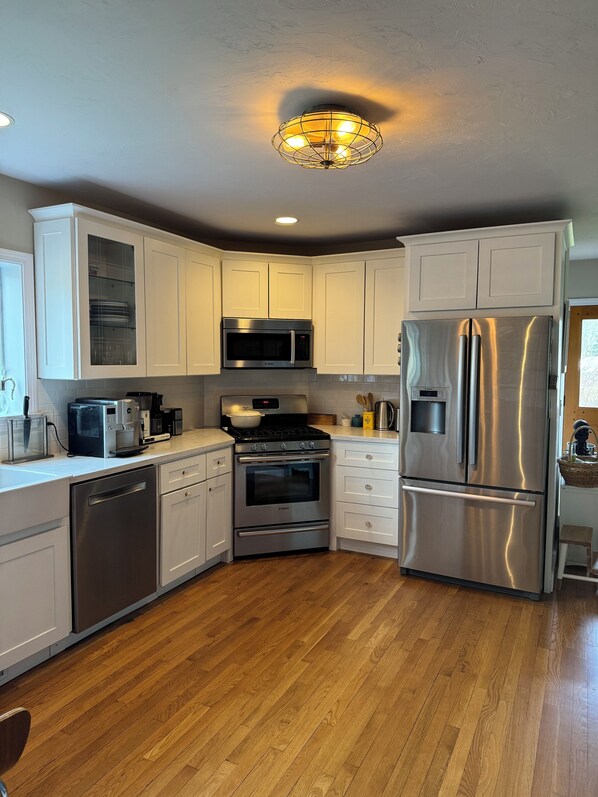 A modern kitchen with white cabinets, stainless steel appliances, and a wooden floor.